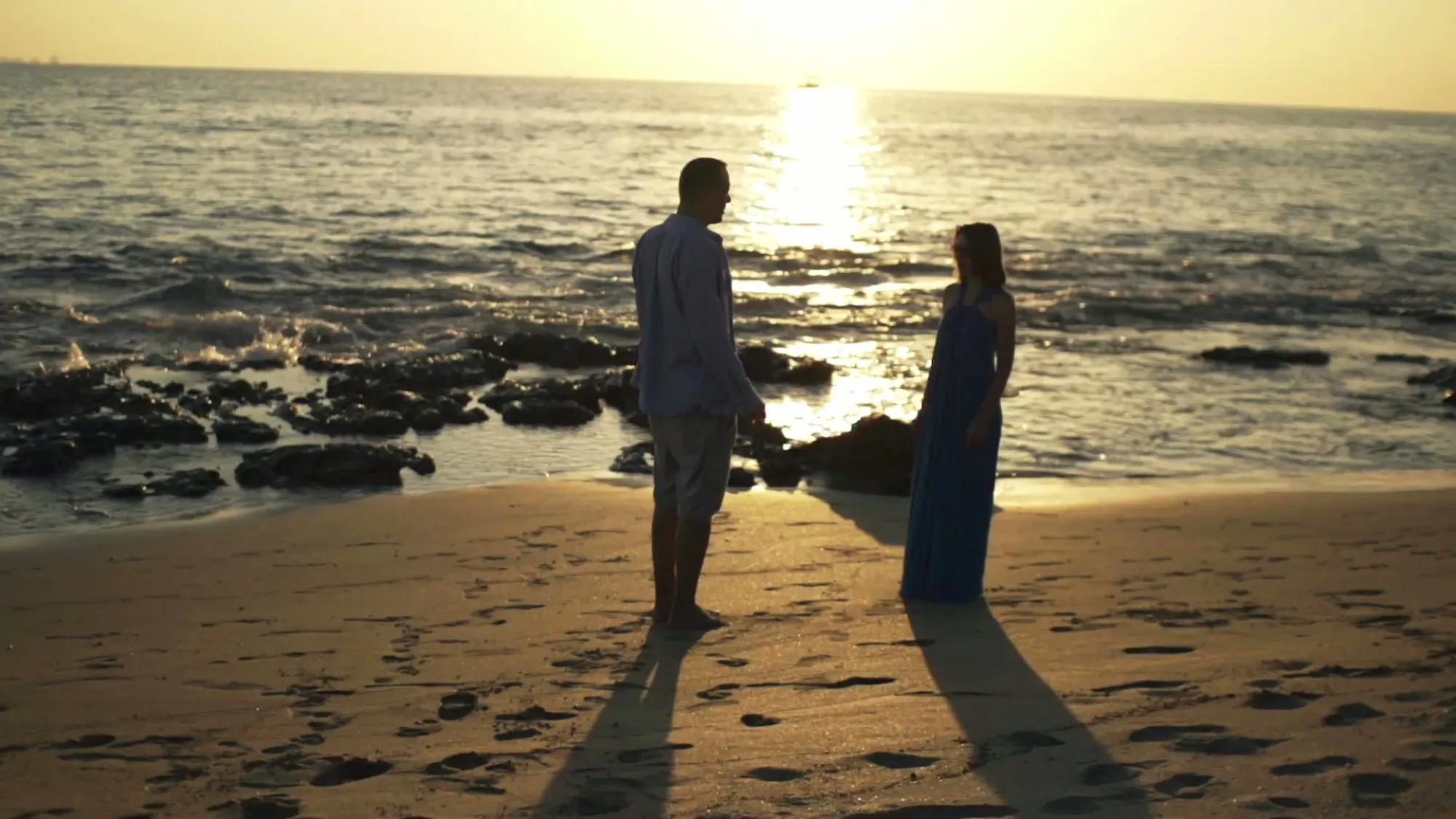 Two people walking apart along a beach at sunset